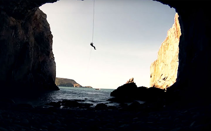 climbing down by rope from a cliff into a cave