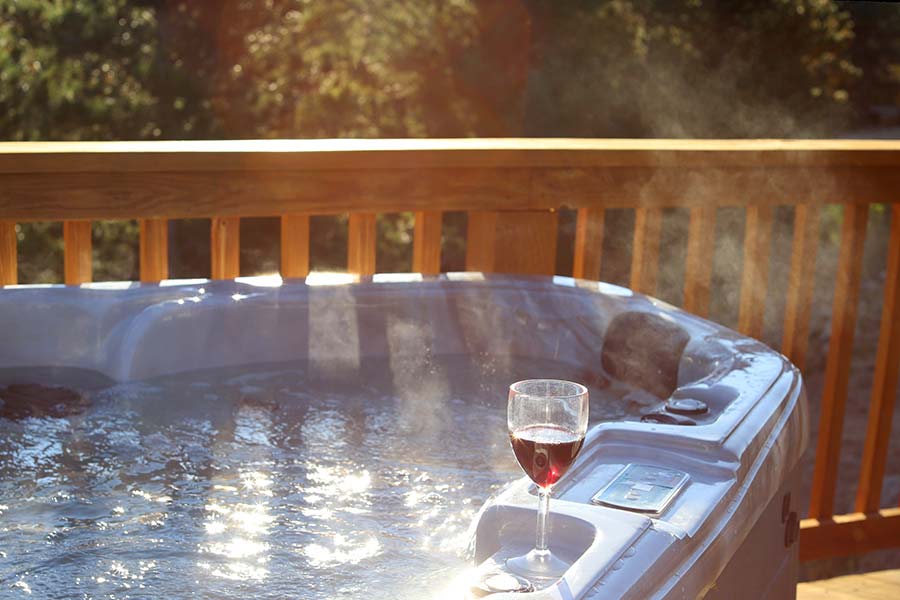 steaming hot tub with wooden fence and glass of red wine on the side