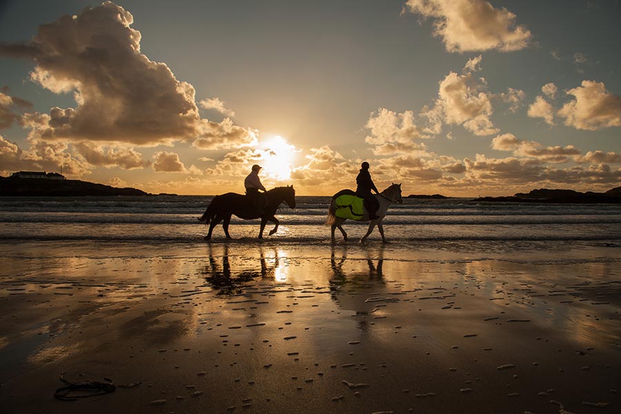Trearddur Bay beach with 2 people on horseback with the sun setting in the background