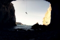 view from inside a cave of a climber coming down from a cliff over the sea